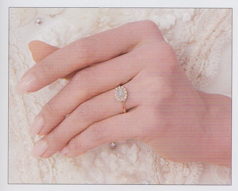 A closeup of Aono Yuuki's hand. She has a natural pink manicure and wears a small gold ring with tiny crystals and a white stone.