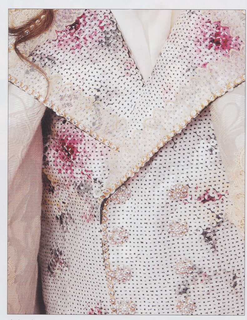 A closeup of Kiriya Hiromu's vest. It is covered with a mosaic of sequins making a pattern of subtle pastel roses. There are lace accents on the lapels.