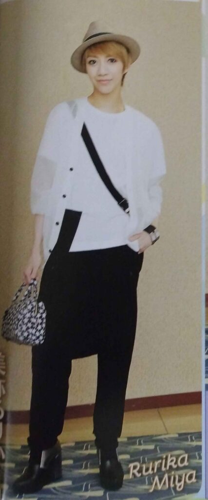 Miya Rurika wearing a beige hat, loose white shirt with black belt over a white tee, black pants and shoes, and holding a small grey bag.