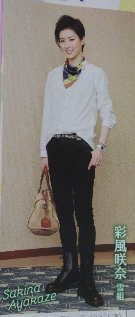 Ayakaze Sakina wearing white shirt, black pants, and lace-up black ankle boots, with brightly striped bandana, silver belt, and tan purse.