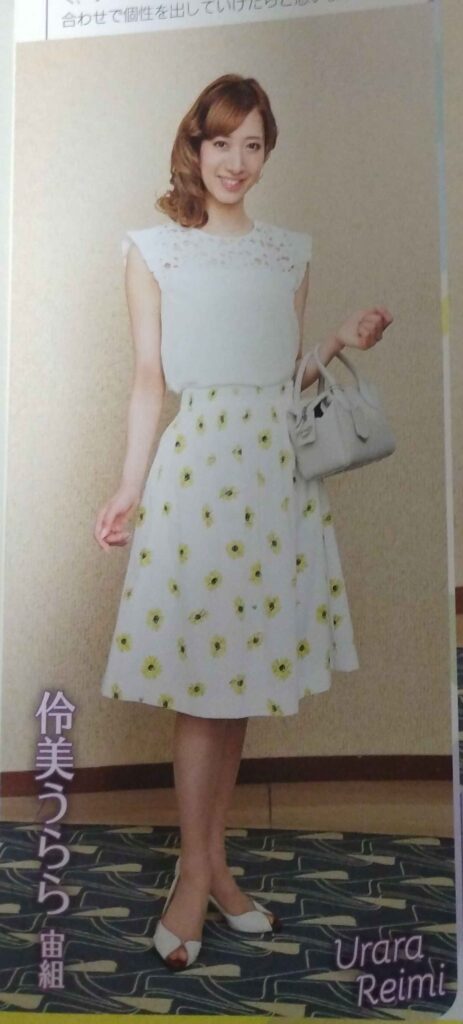 Urara Reimi wearing white sleeveless blouse with sheer lace, white knee length skirt with sunflowers, white peep toe shoes, and small tan purse.