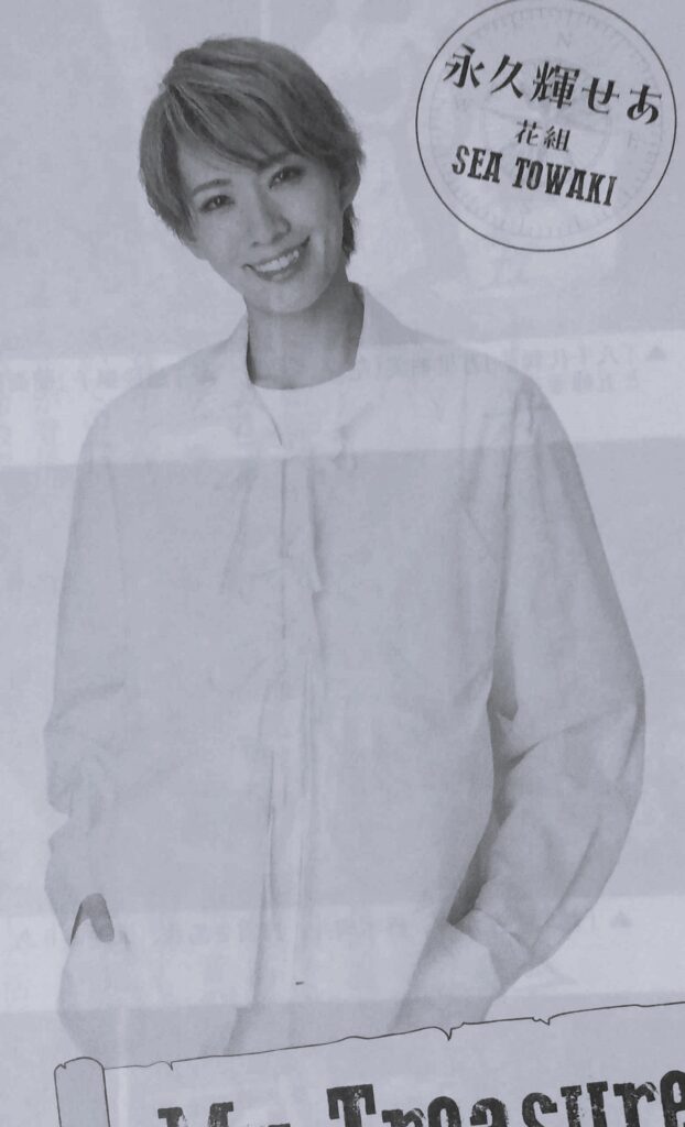 Towaki Sea smiling at the camera. She is wearing a loose white long-sleeve shirt with a ruffled collar.