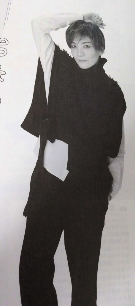 Houzuki An posing with one arm over her head. She is wearing an asymmetrical black vest over a white shirt.