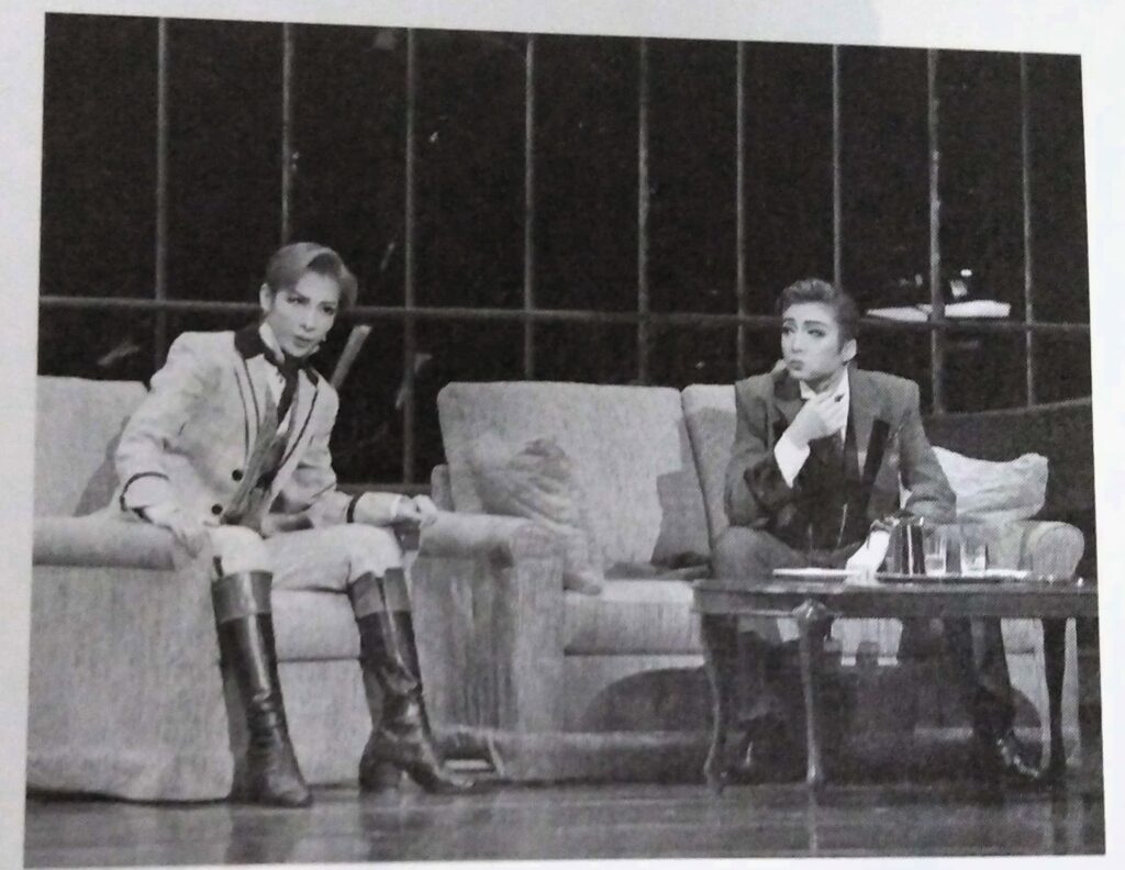 A stage photo of Houzuki and Asumi Rio in Ernest in Love, Houzuki is in the middle of eating a plate of cucumber sandwiches.